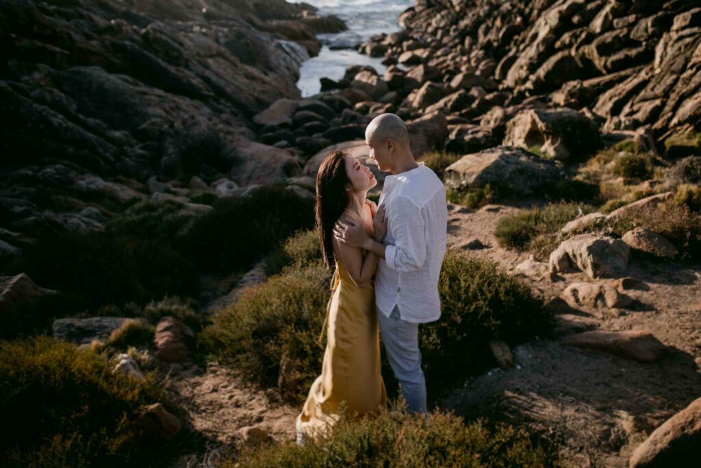 Couple sharing a tender moment in the rugged coastal landscape of Injidup Spa Retreat, photographed by Moments by Naz in Western Australia