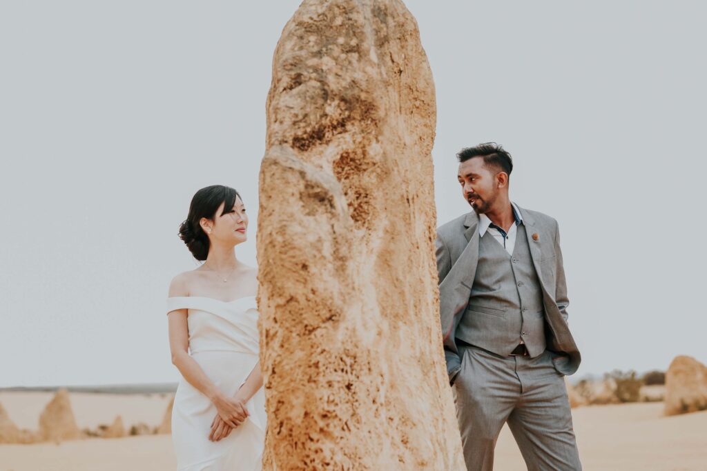Bride and groom sharing a playful moment behind a limestone formation during their pre-wedding photo shoot at the Pinnacles Desert in Western Australia.
