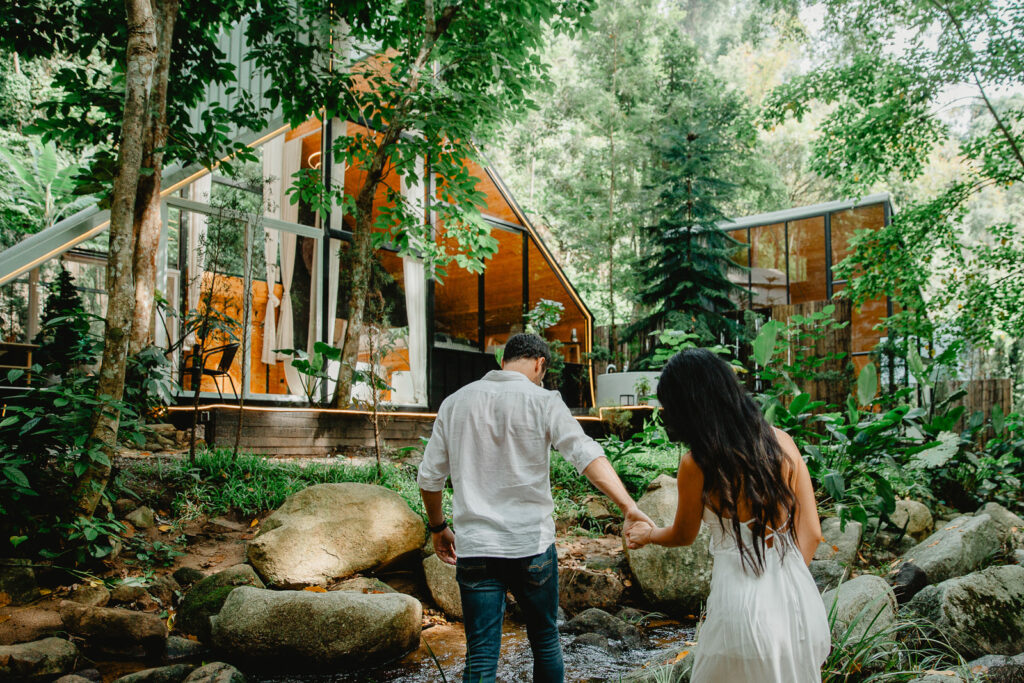 Couple walking hand in hand through the forest near their glass cabin during a Thailand honeymoon and elopement in Chiang Mai. with elopement photographer moments by naz