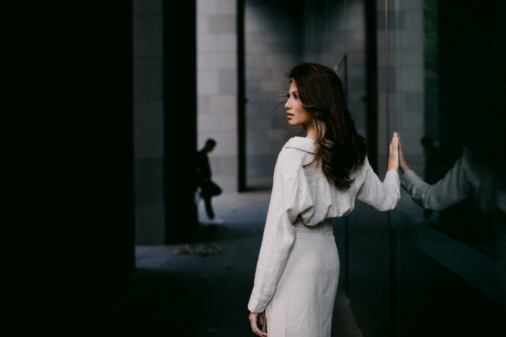 Bride-to-be in soft linen outfit leaning on reflective glass during a Perth city pre-wedding shoot.