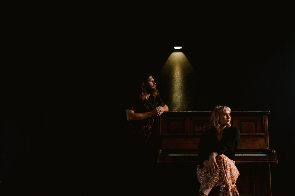 Indoor pre-wedding shoot in Perth with couple by a vintage piano under dramatic lighting.