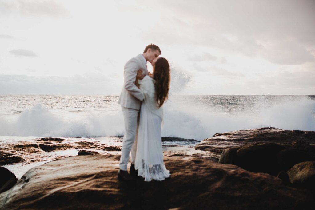 just married couple kissing at conto beach with wave crashing behind them for the elopement session in margaret river