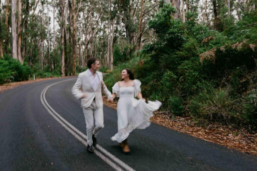 couple running together down caves road for their destination pre-wedding photos in Perth, Boranup forrest margaret River