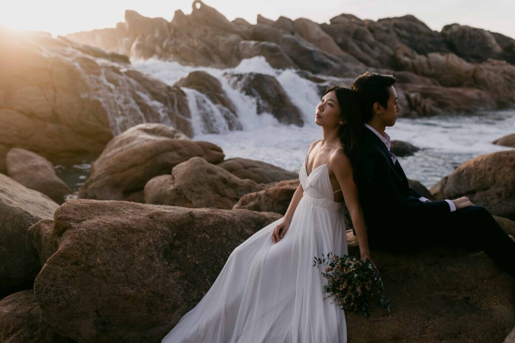 sunset in the background couple sitting back to back for their pre-wedding photos at injidup spa