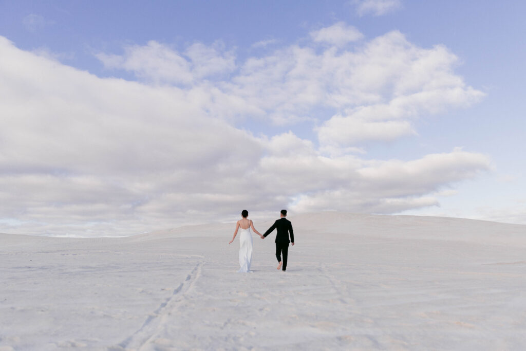 Joey and Davis walking beneath a dramatic sky during their Lancelin pre-wedding shoot