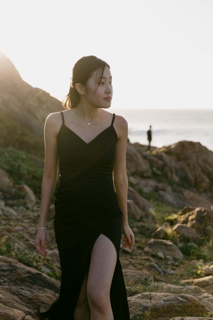 Joey in a black dress among the coastal rocks with Davis in the distance