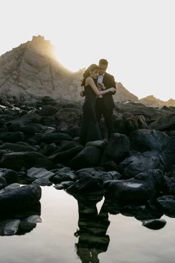 Joey and Davis embracing beside a rock pool as the sun sets behind Sugarloaf Rock