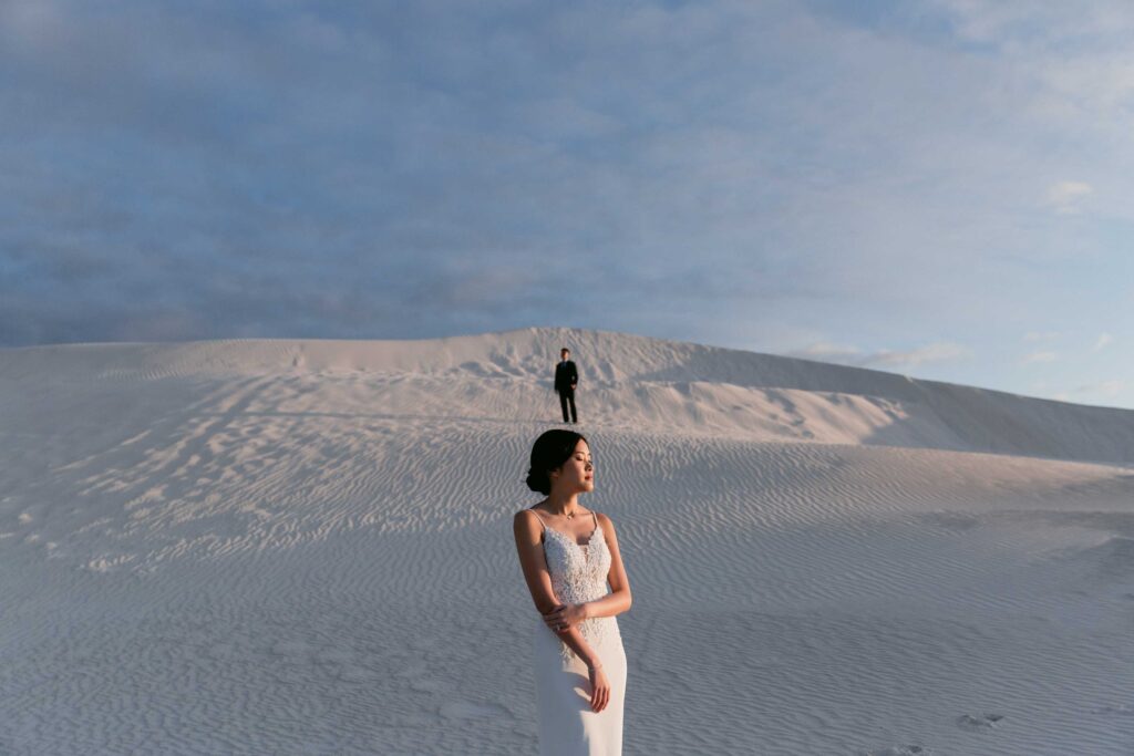 Joey standing in the foreground with Davis high on a dune behind her at Lancelin