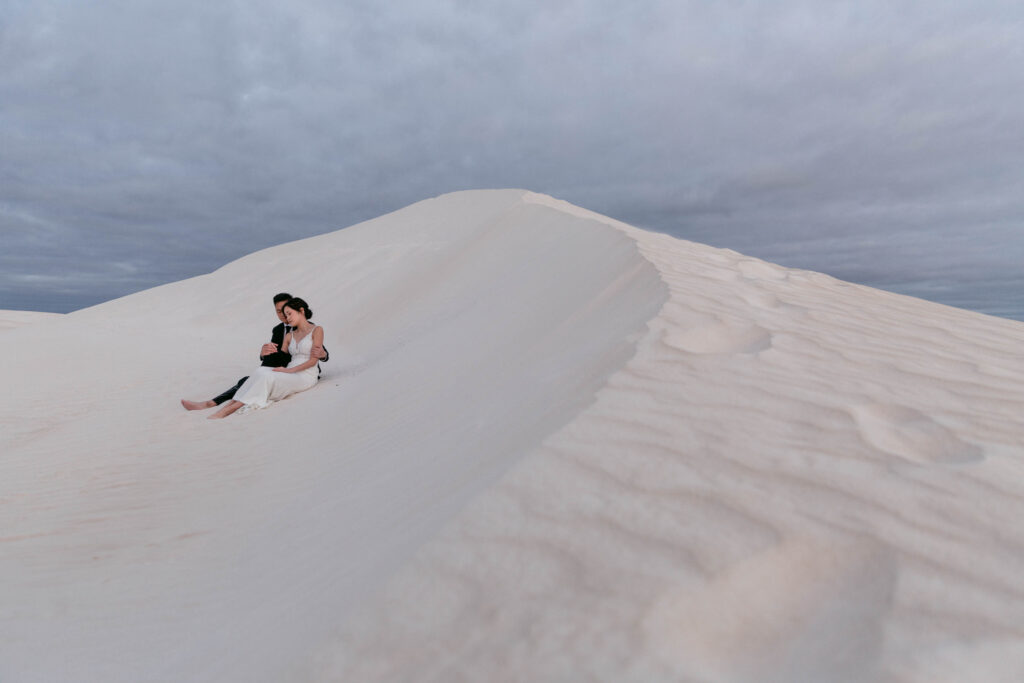 Joey and Davis sitting together on the crest of a white sand dune at Lancelin