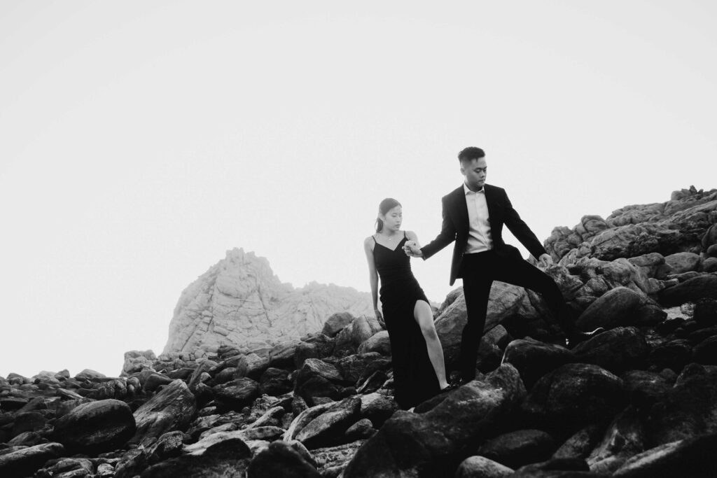 Joey and Davis walking across coastal rocks with Sugarloaf Rock behind them