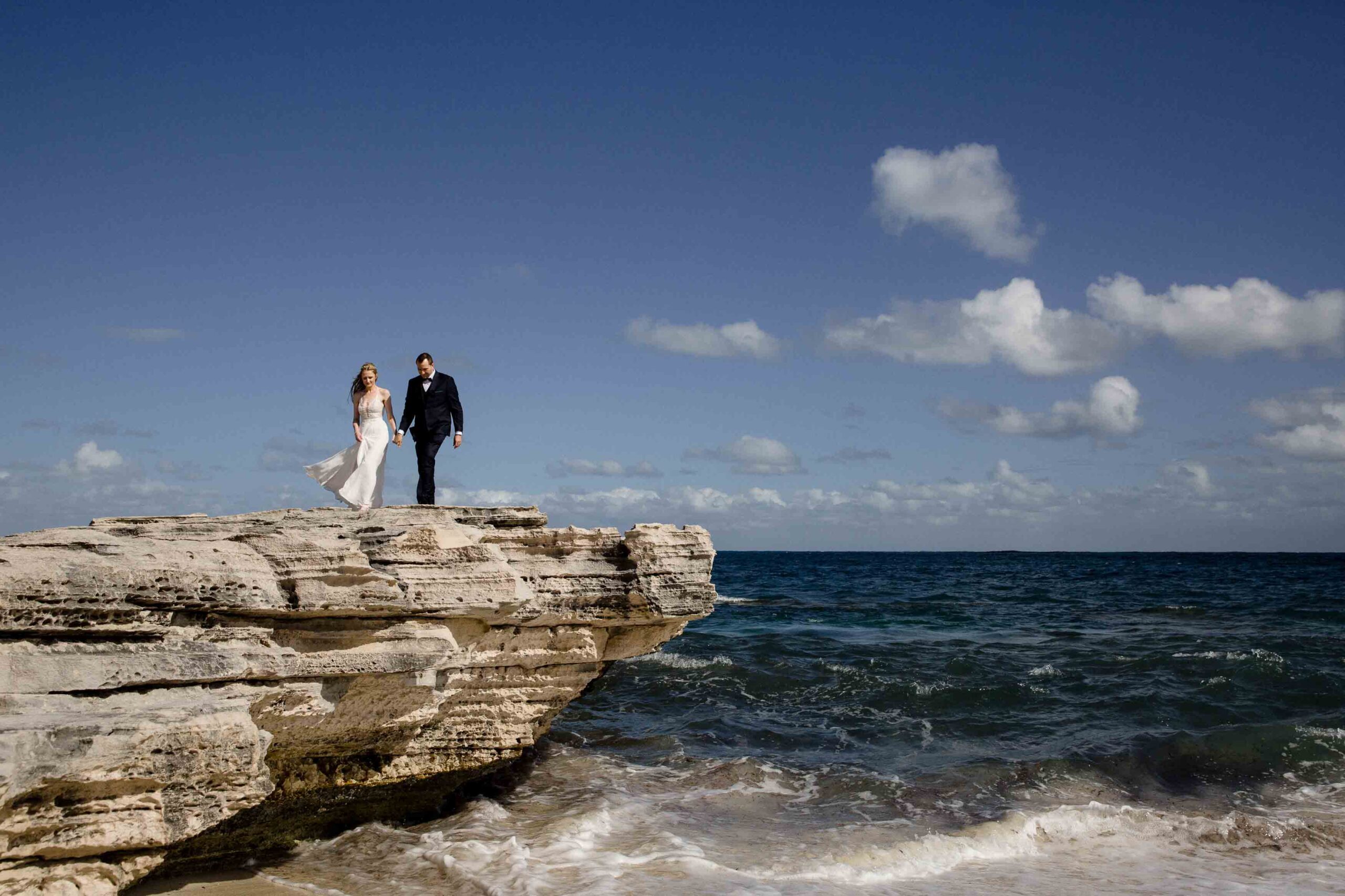 Couple in wide shot walking on rocky coastline on rottnest island after the micro-wedding in Perth